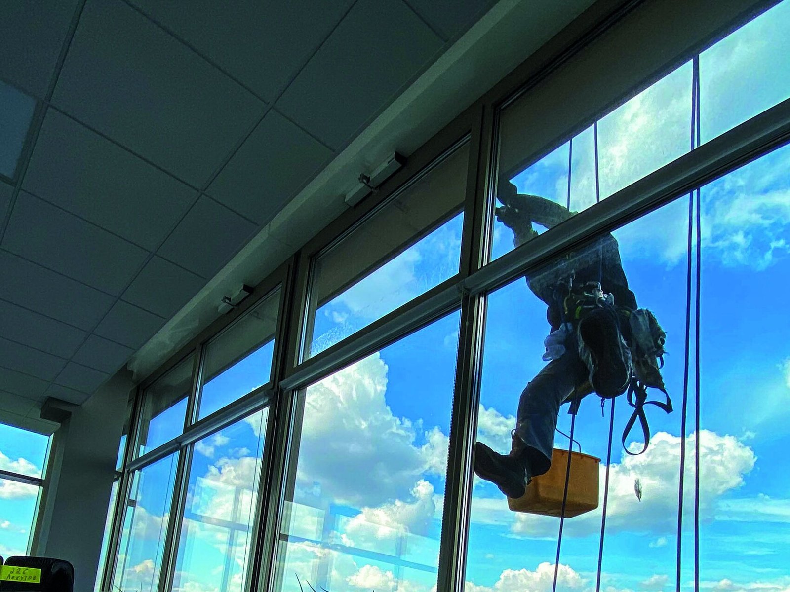 A technician on rope seen through the glass from inside a building